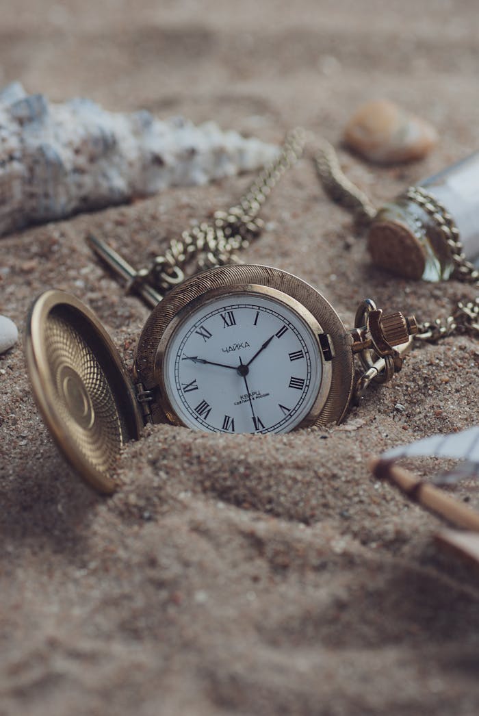 A classic gold pocket watch partially buried in sand, exuding timeless elegance and a sense of nostalgia.